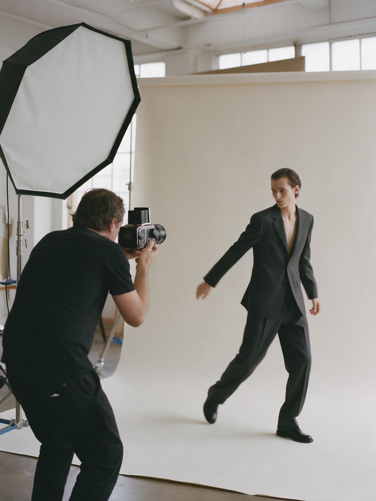 Photographer shooting a model in a charcoal suit on a white cyclorama