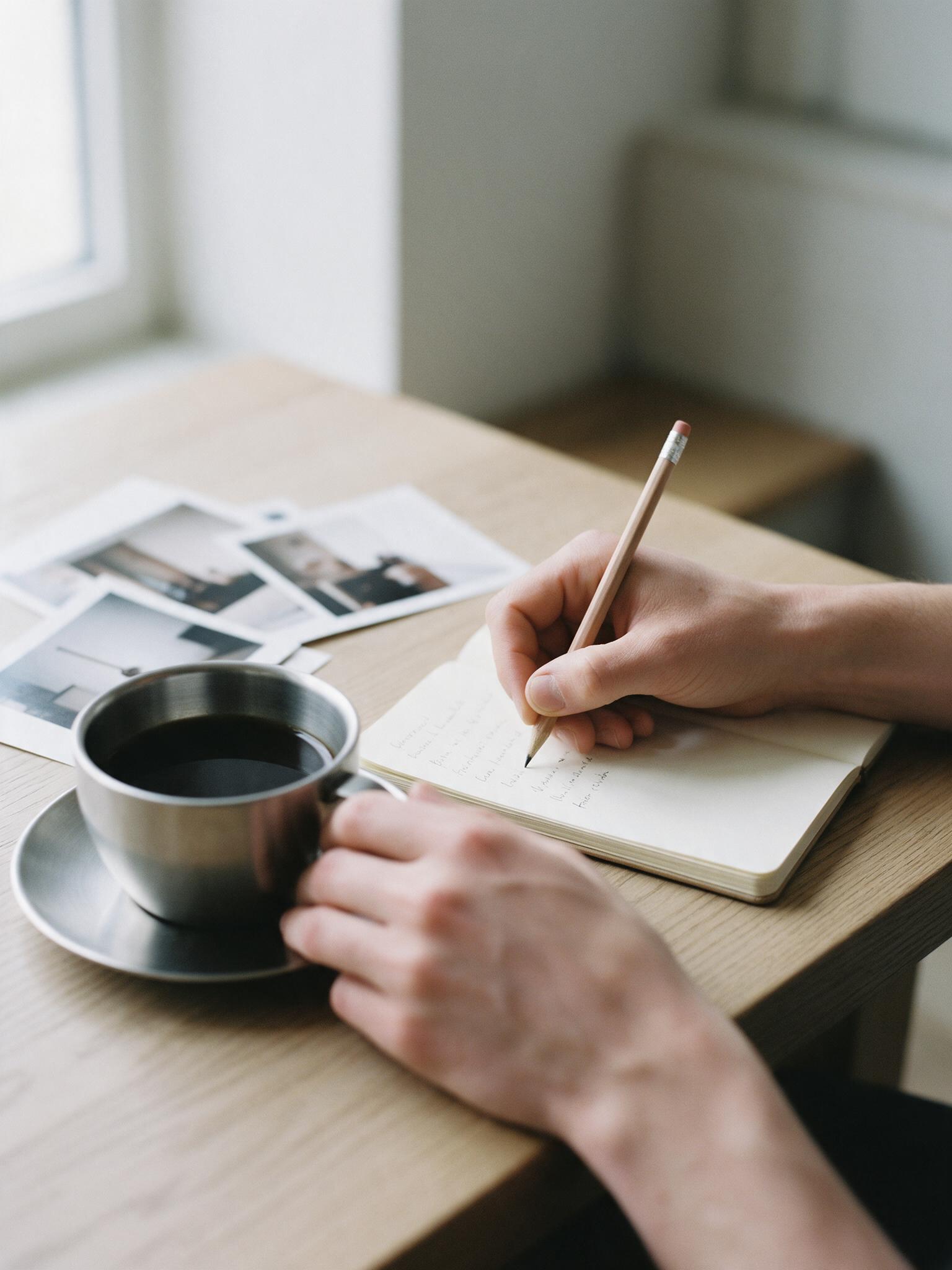 Hands taking notes in a notebook beside a black coffee during a meeting